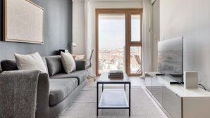 A modern living room with a grey sofa, a coffee table, a TV, and a city view through the window. - Deluxe Favoriten 1BR w/ Roof, Gym & Lounge, 1min to HBF, by Blueground (Vienna)