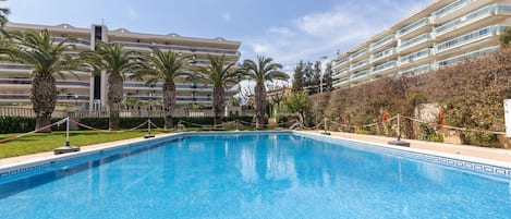 A swimming pool surrounded by palm trees and a multi-story hotel building.