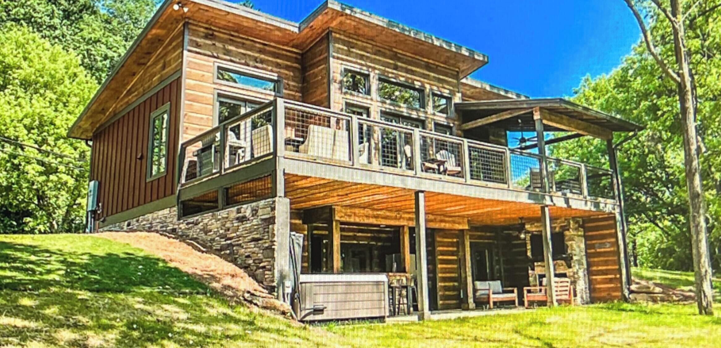 Une cabane en rondins à deux étages, dotée d’un balcon, de fondations en pierre et d’un espace extérieur couvert aménagé en coin salon.