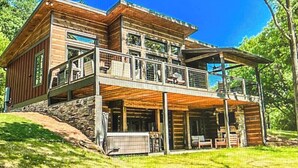 Eine zweistöckige Blockhütte mit Balkon, Stein Fundament und einer überdachten Sitzgelegenheit im Freien.