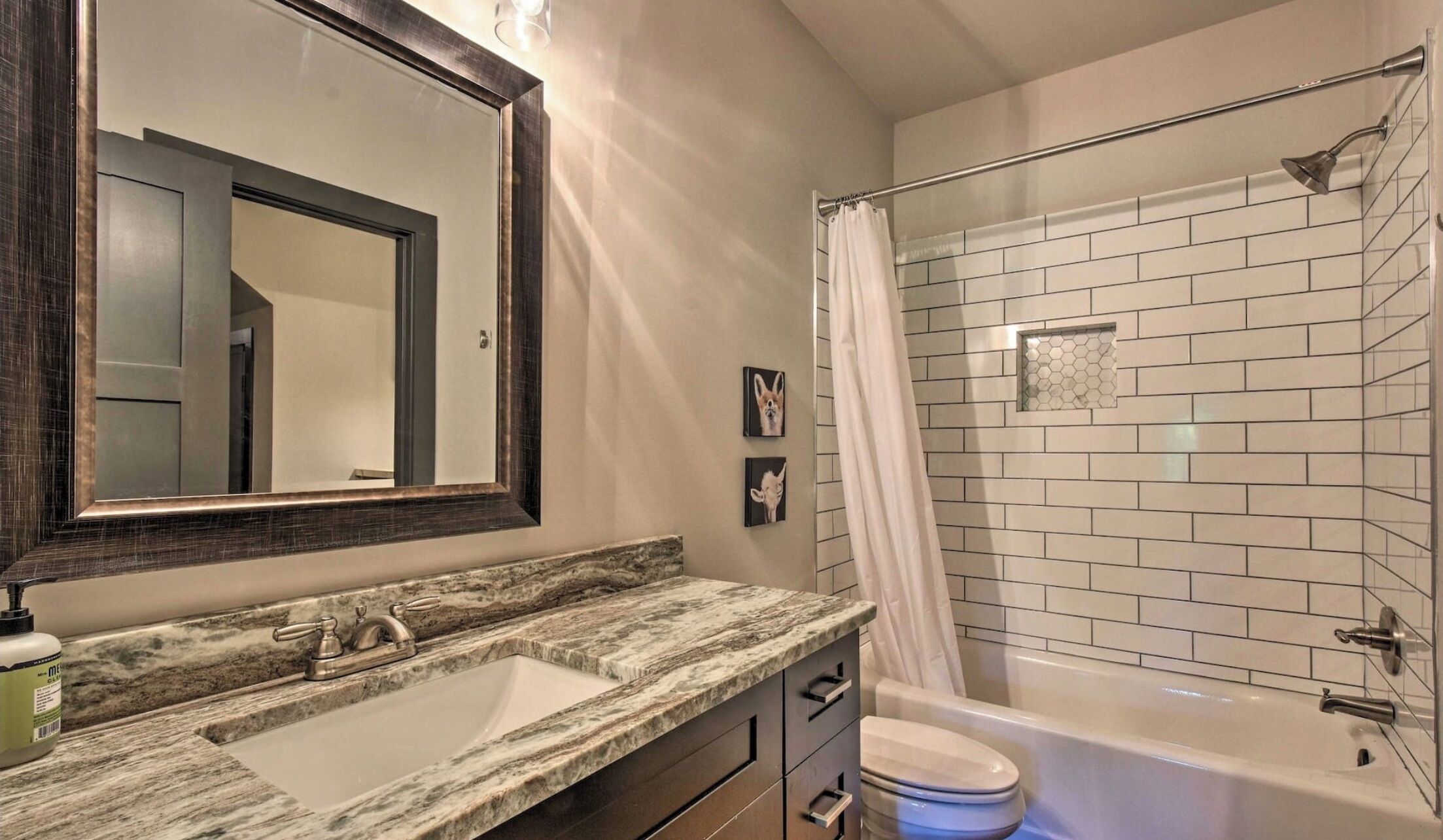 Une salle de bain avec un lavabo en marbre, un grand miroir, une douche avec une porte en verre et un mur recouvert de carreaux blancs.