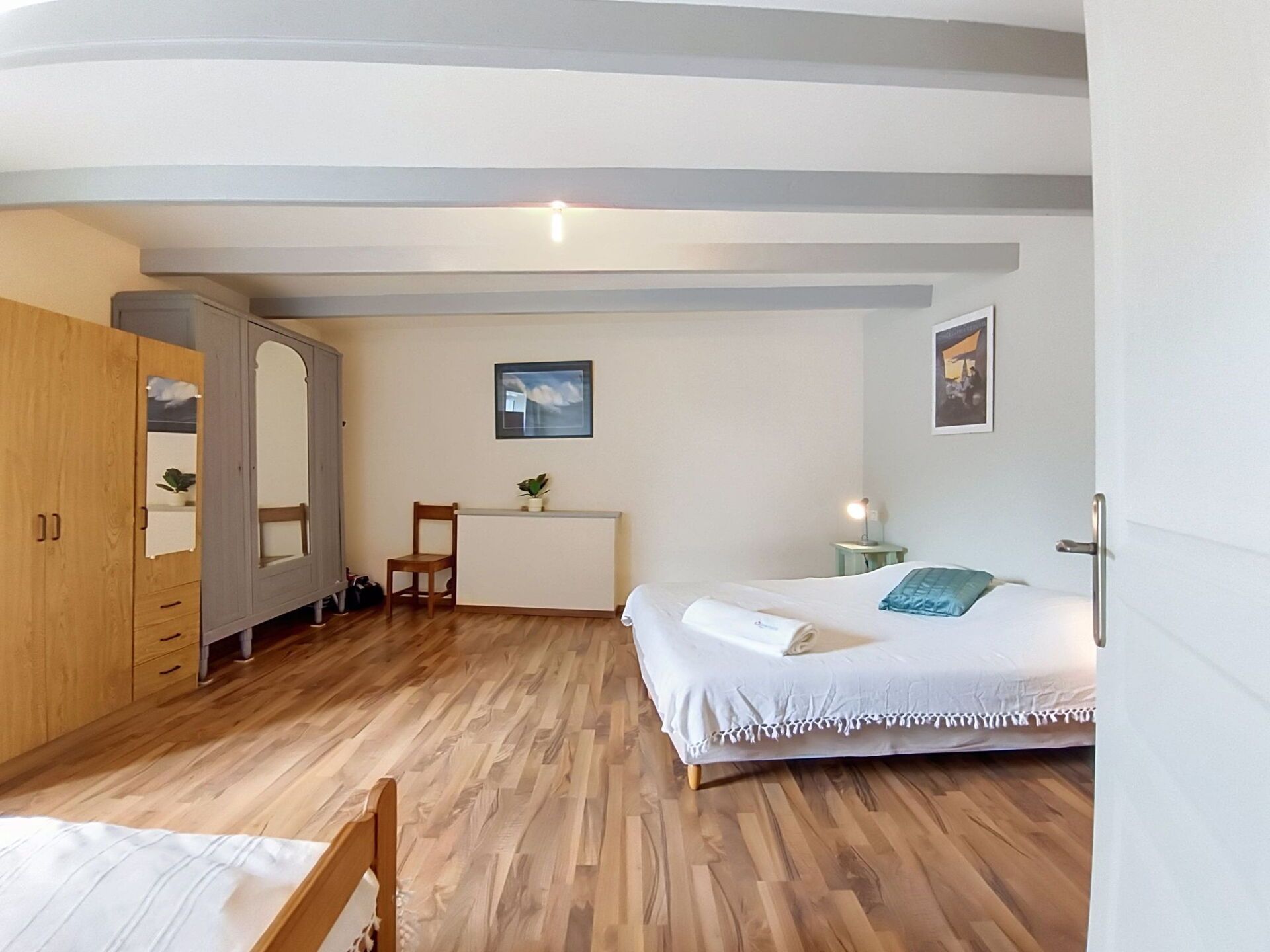 Une chambre avec un plancher en bois, un lit, un bureau, une chaise et une armoire.