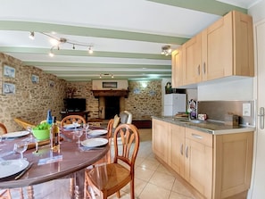 Zona pranzo con parete in pietra, sedie di legno, tavolo apparecchiato per quattro e cucina con mobili in legno e forno a incasso.