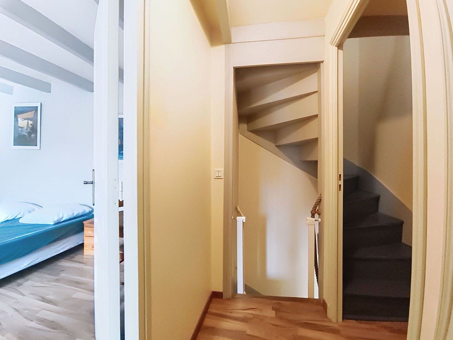 Un corridoio che porta a una scala con pavimento in legno e un letto nella stanza adiacente.