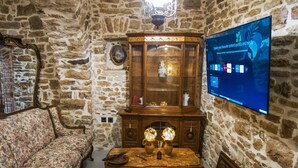 A room with stone walls, a wooden cabinet with glass doors, floral-patterned furniture, and a television mounted on the wall. - Albanian Coast - House - Stay 9 - Hottub - Petsok (Himarë)