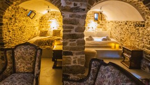 A stone-walled room with a bed, two chairs, a small table, and a hanging light fixture. - Albanian Coast - House - Stay 9 - Hottub - Petsok (Himarë)