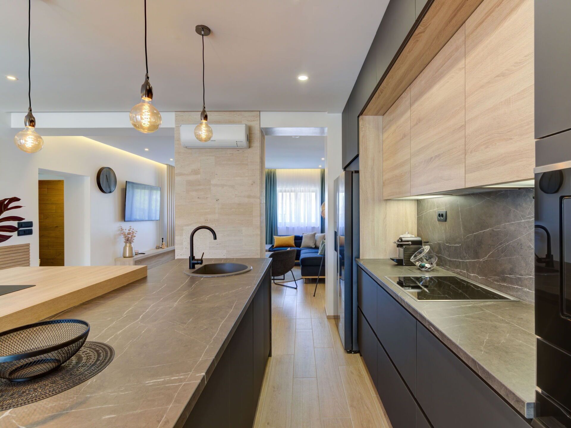 A modern kitchen with a central island, pendant lighting, and a view into the living area.