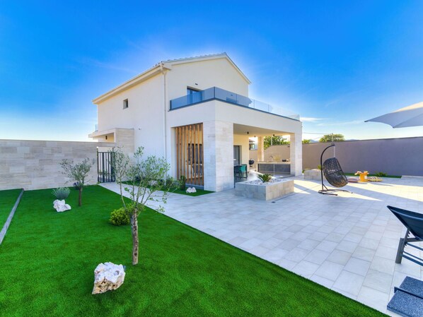 A modern house with a patio, a small garden, and a hanging chair.