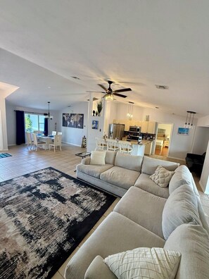 A spacious living room with a large sectional sofa, a dining area with a table and chairs, and a kitchen in the background.