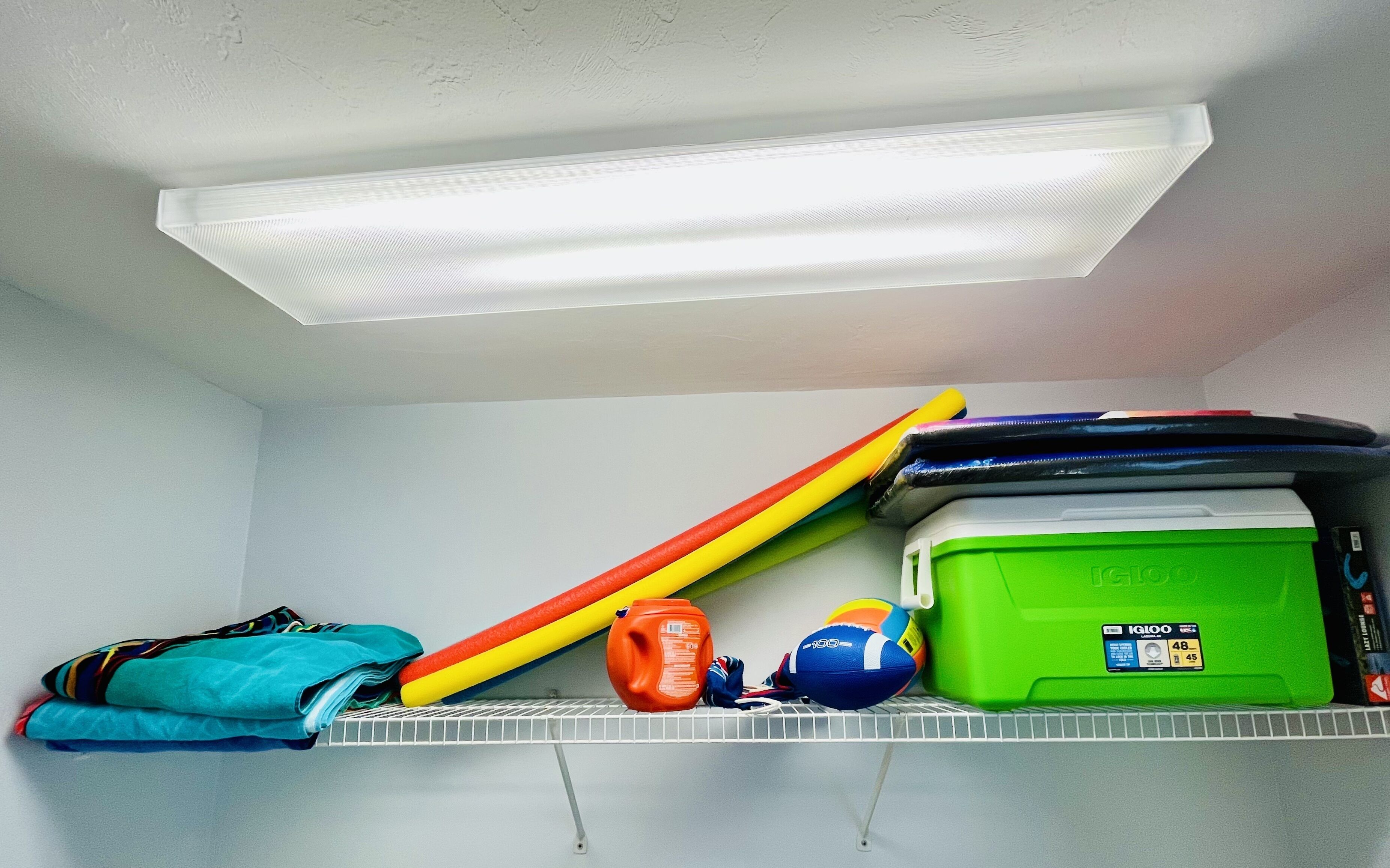 A storage shelf with folded clothes, a green storage box, and sports equipment.