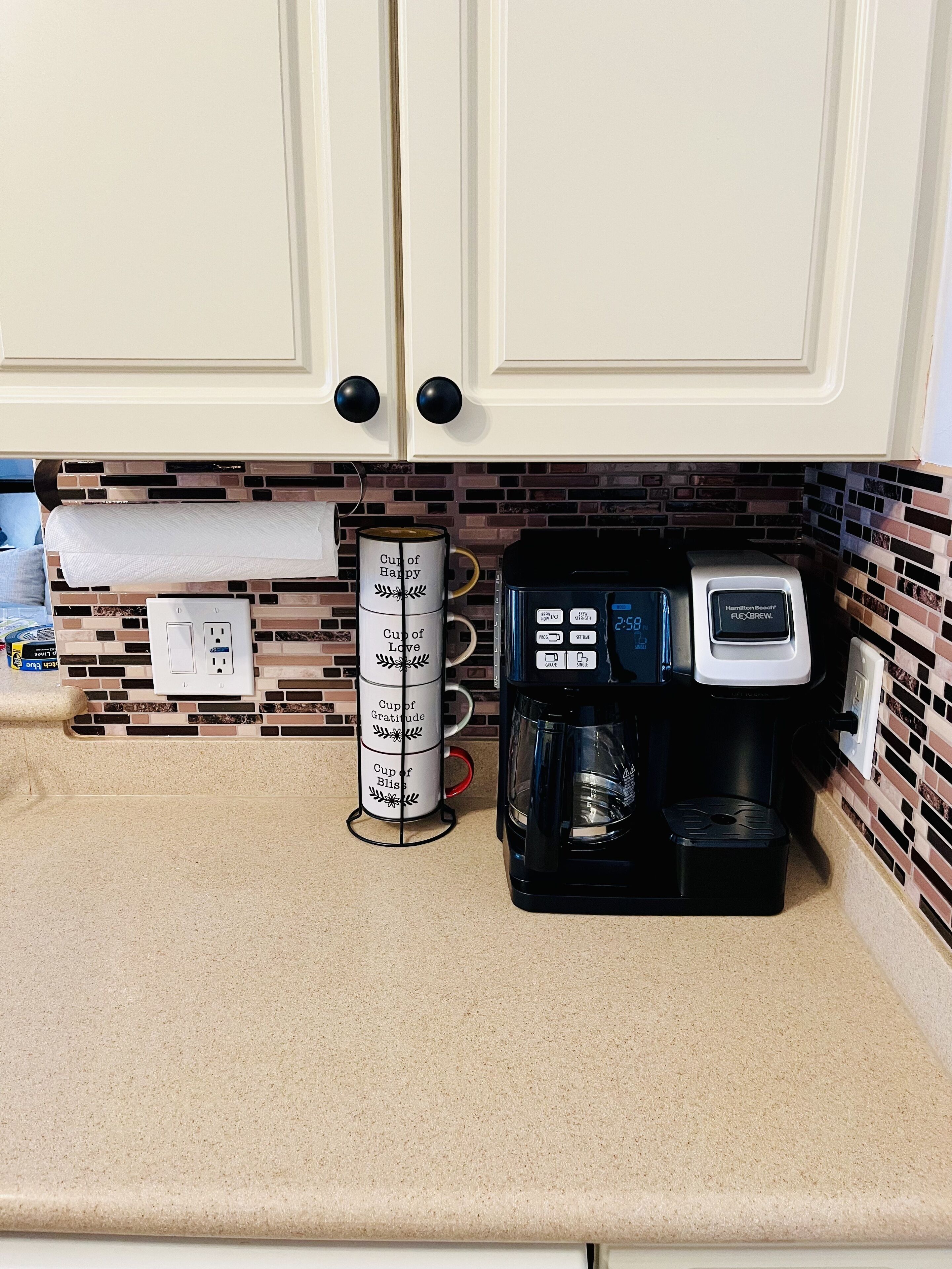 Cozinha com armários brancos, cafeteira e suporte para chávenas.