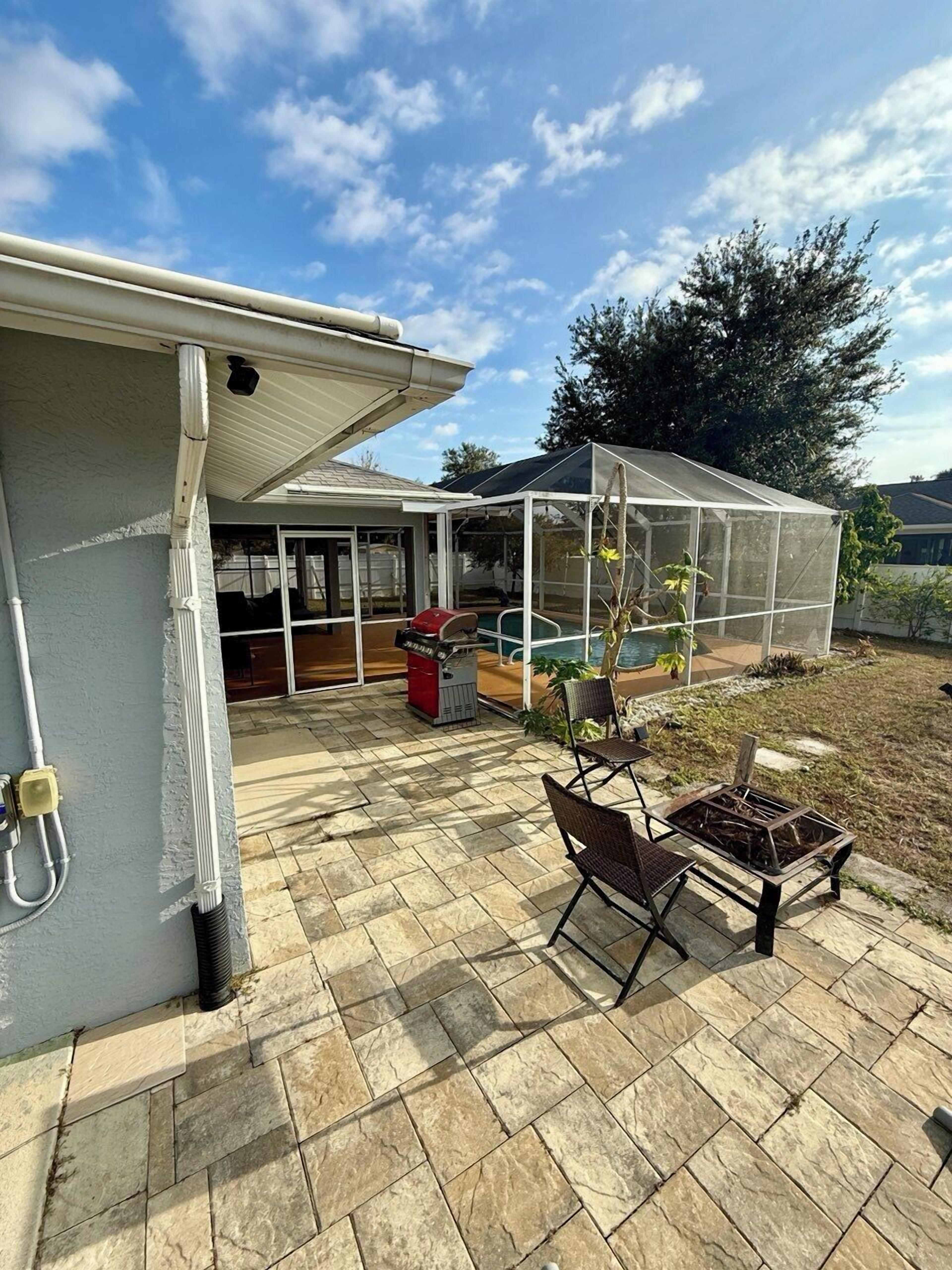 A backyard with a covered patio, a pool, and a greenhouse.