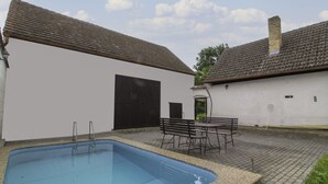 Une piscine avec une terrasse carrelée, un espace salon couvert et un bâtiment blanc avec une porte noire.