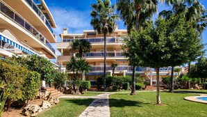 A multi-story hotel with a stone pathway leading to a pool area, surrounded by well-maintained lawns and palm trees.