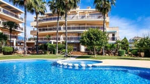 A multi-story hotel with a swimming pool surrounded by palm trees and greenery.