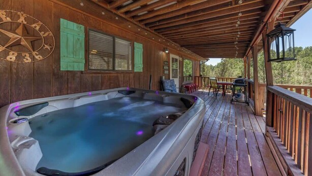 Een hottub op een houten terras met houten afdak, een kompasbord en uitzicht op bomen.