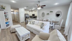 A spacious living room with a white sofa, a wooden coffee table, and a dining area with a wooden table and white chairs.