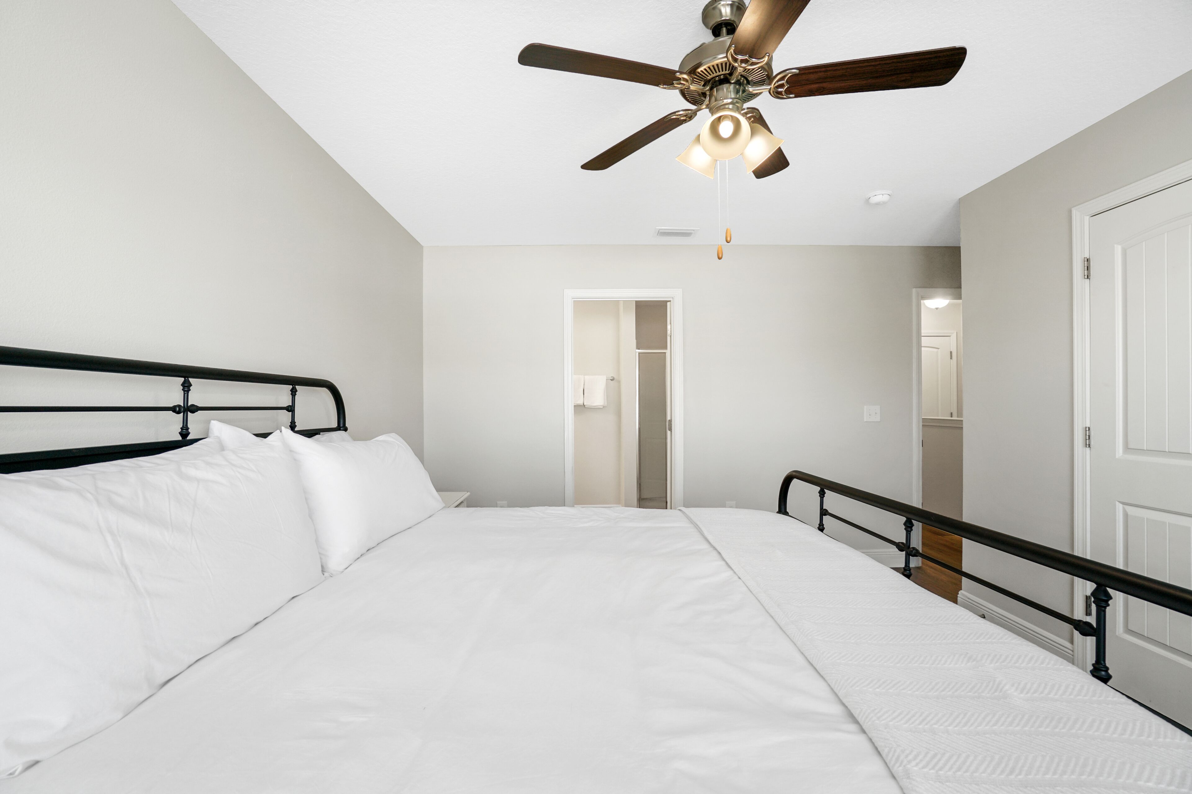 A bedroom with a large bed, a ceiling fan, a door, and a white wall.