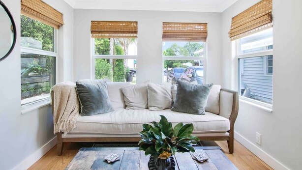 A cozy room with a beige sofa, two windows with blinds, and a wooden coffee table with a plant.