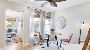 A room with a round table, two chairs, a ceiling fan, and a decorative wall piece.