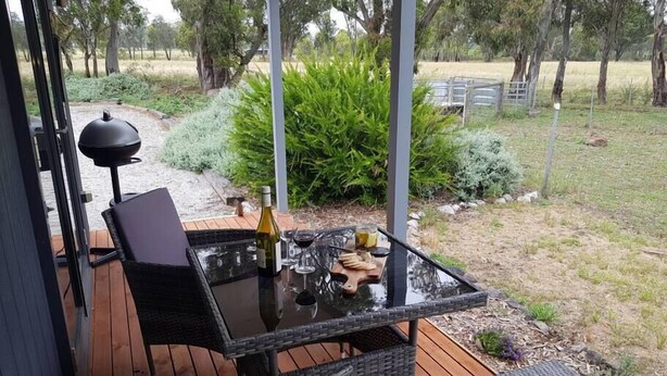 Een terras buiten met een glazen tafel, rieten stoelen en een fles wijn.