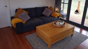 Een moderne woonkamer met een donkere bank, twee kussens, een houten salontafel met een plant, en een lijst met een foto aan de muur.