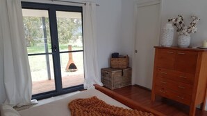 Een slaapkamer met een groot bed, een houten dressoir en uitzicht door een schuifdeur op een terras.