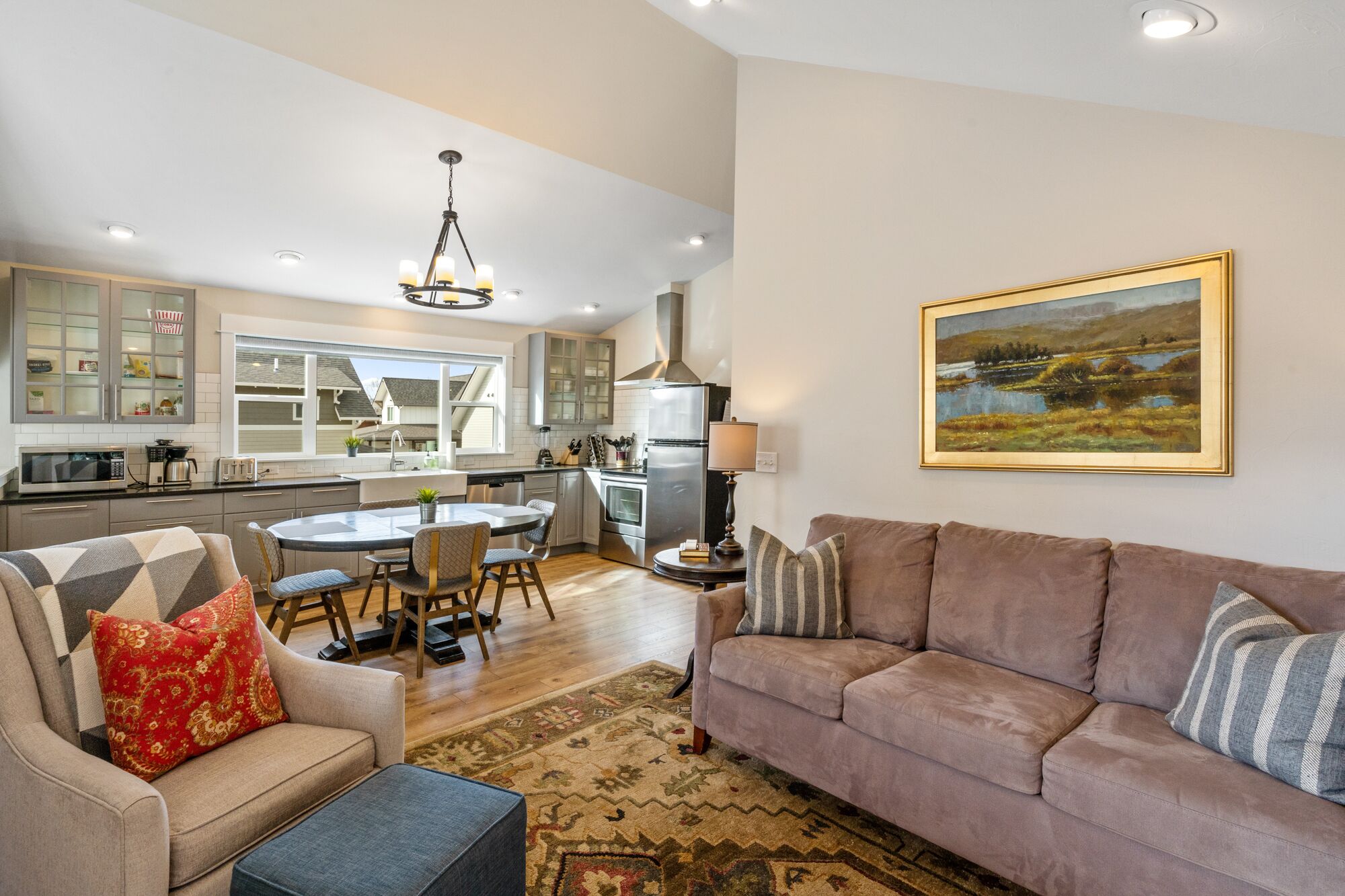 A modern kitchen with a dining area, a sofa, and a painting on the wall.
