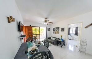 A spacious living area with a dining table, chairs, a sofa, and a ceiling fan. - Lovely Palms Condo short distance to beaches (Sosúa)