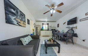 A living room with a sofa, coffee table, and a dining area with chairs and a table. - Lovely Palms Condo short distance to beaches (Sosúa)