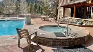 A pool area with a hot tub, wooden deck, stone wall, and a view of mountains. - Luxury 3 Bedroom Mountain Townhome in Keystone (Dillon)