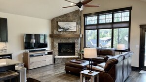 A spacious living room with a stone fireplace, a large window, and a modern entertainment unit. - Luxury 3 Bedroom Mountain Townhome in Keystone (Dillon)