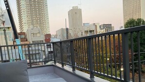 A rooftop terrace with a sofa and a glass table, overlooking a cityscape with modern buildings. - Asakusa HomeSuites Tokyo (Tokyo)