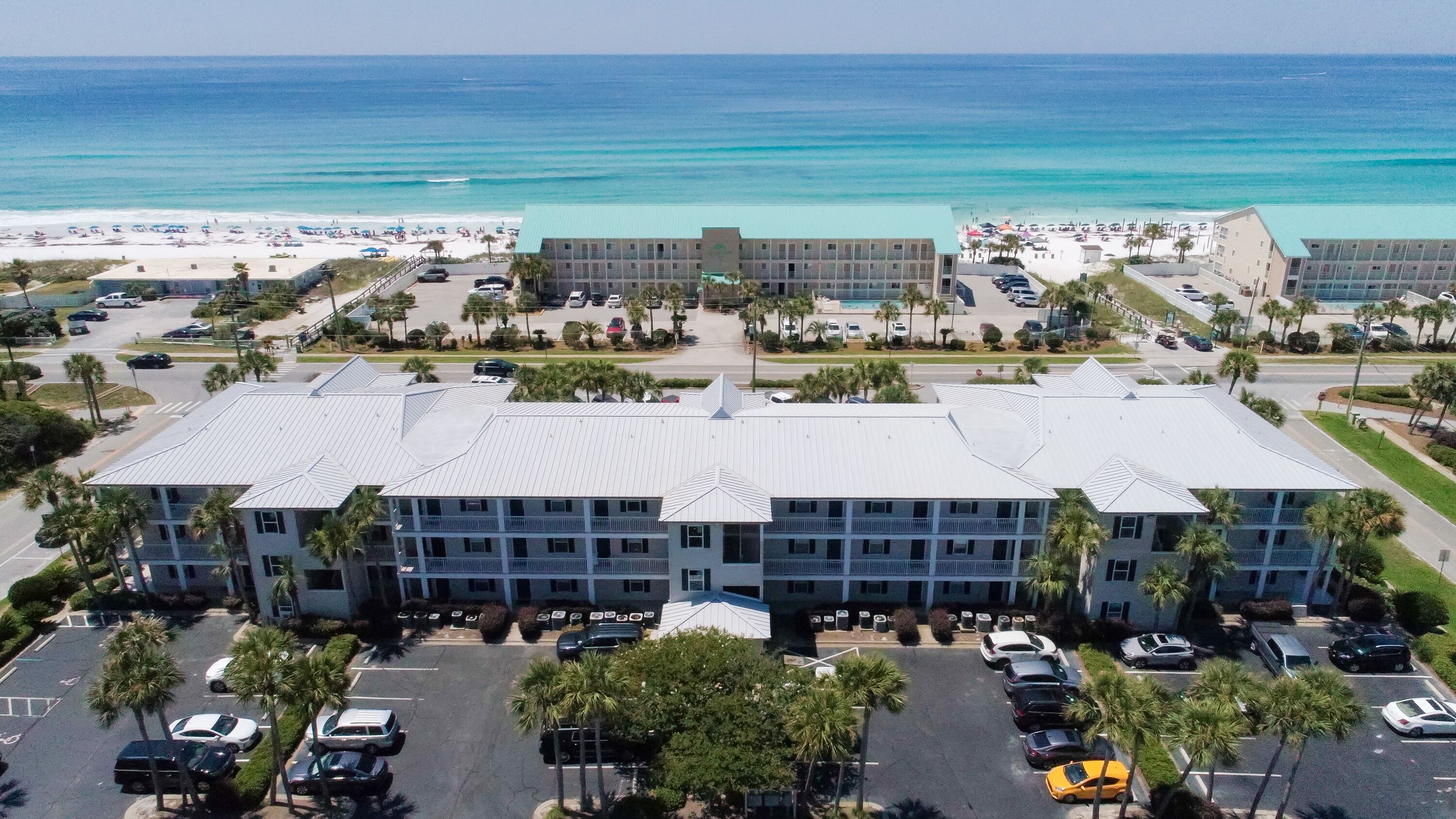 A multi-story hotel with a flat roof, parking lot, and a beach view.