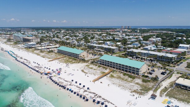 Eine Luftaufnahme einer Küstenstadt mit Strand, Gebäuden und blauem Himmel.