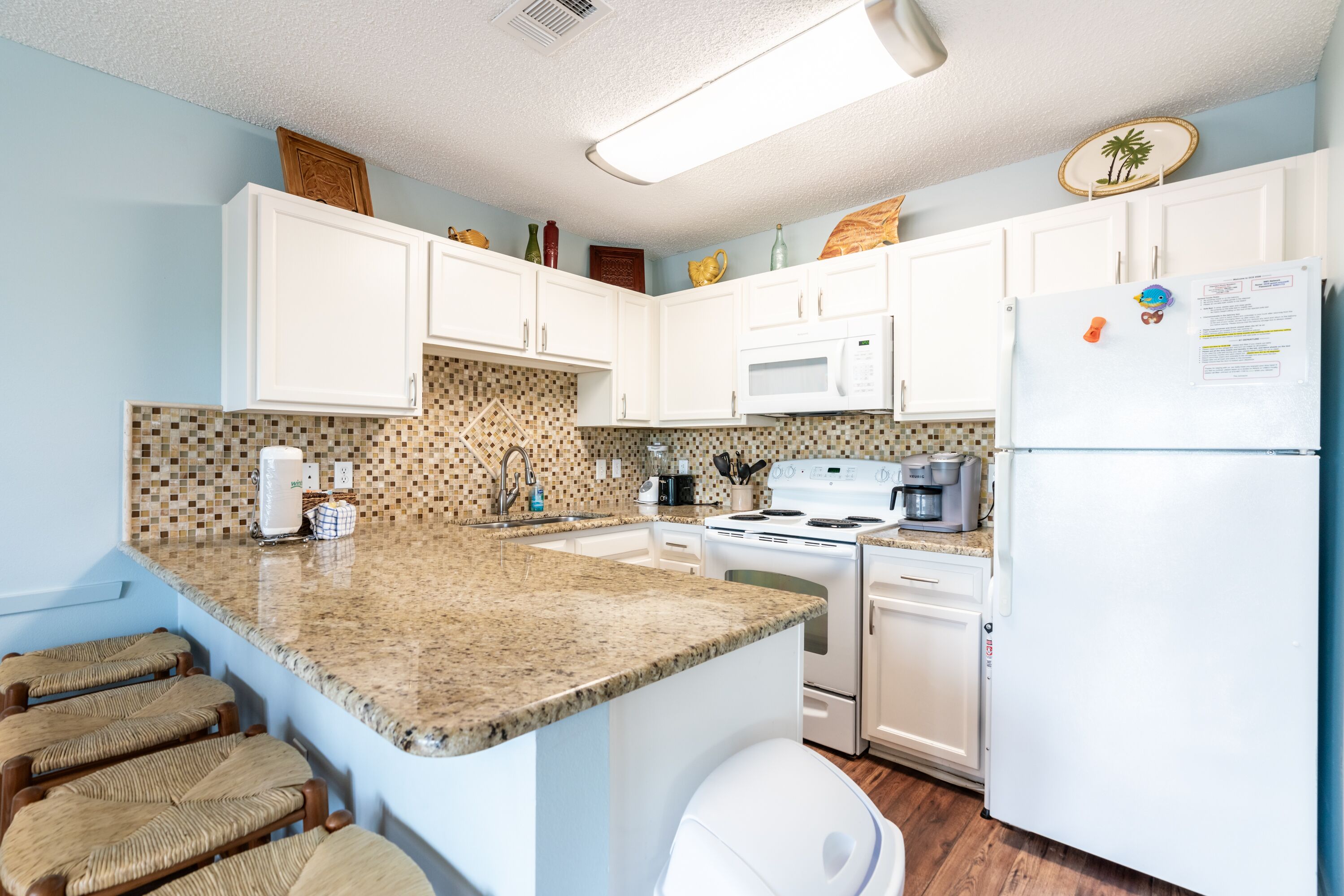 A kitchen with white cabinets, a granite countertop, a white refrigerator, and a microwave.