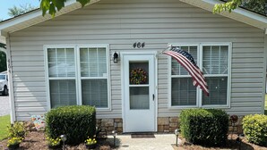 Une maison de plain-pied avec une porte d’entrée, deux fenêtres et un drapeau américain sur le côté droit.