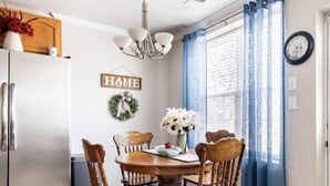 Un coin repas avec une table et des chaises en bois, un lustre, un réfrigérateur et un panneau indiquant « MAISON » sur le mur.