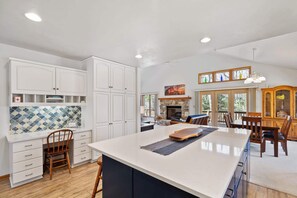 A spacious kitchen with white cabinetry, a large island, and a stone fireplace.