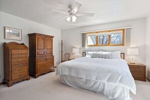 A bedroom with a bed, a wooden dresser, a ceiling fan, a window with a view, and a coat rack. - Blue Skies and Cherry Pies, in Fish Creek! (Fish Creek)