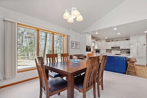 A modern kitchen with white cabinets, a blue island, and a dining area with a wooden table and chairs. - Blue Skies and Cherry Pies, in Fish Creek! (Fish Creek)