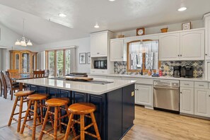 A modern kitchen with a central island, bar stools, a dishwasher, and a large window.
