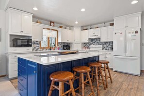 A kitchen with white cabinets, a central island with stools, a microwave, and a refrigerator.
