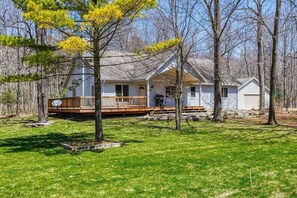A two-story house with a porch, surrounded by trees and a grassy yard. - Blue Skies and Cherry Pies, in Fish Creek! (Fish Creek)