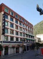 Un hotel de varios pisos con una hilera de ventanas en cada nivel, un toldo verde sobre la entrada y una montaña al fondo.
