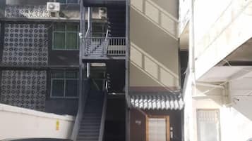 Un edificio de varios pisos con una escalera central, unidades de aire acondicionado exteriores y una entrada con portón.