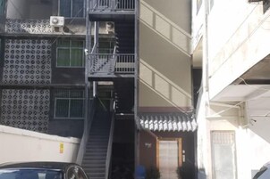 Un edificio de varios pisos con una escalera central, unidades de aire acondicionado exteriores y una entrada con portón.