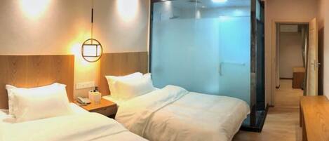A hotel room with two beds, a nightstand, a wall-mounted lamp, and a glass partition.