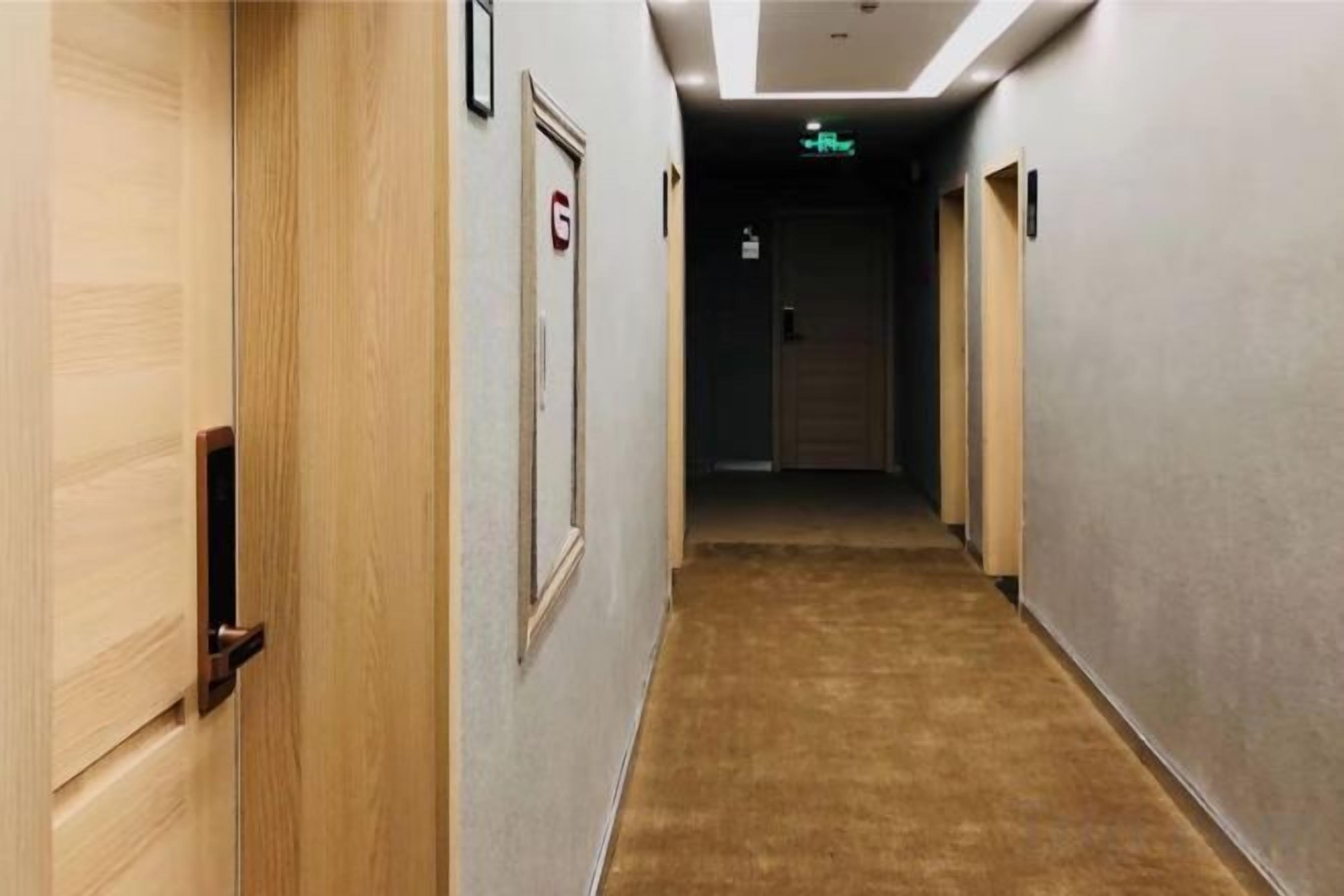 A hotel corridor with wooden doors, a carpeted floor, and a sign indicating a room number.