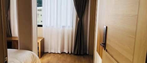 Een hotelkamer met een bed, een houten deur en een raam met gordijnen.